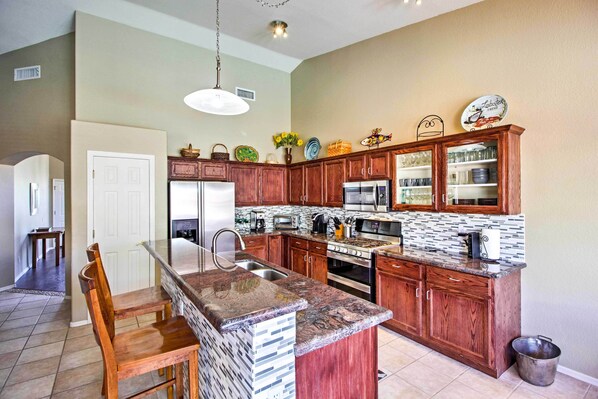A kitchen with wooden cabinets, a granite countertop, stainless steel appliances, and a hanging light fixture. - Tucson Home W/pool & Santa Catalina Mtn Views (Tucson)