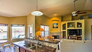 A kitchen with a central island, a dining area with chairs, a sofa, a fireplace, and a television. - Tucson Home W/pool & Santa Catalina Mtn Views (Tucson)