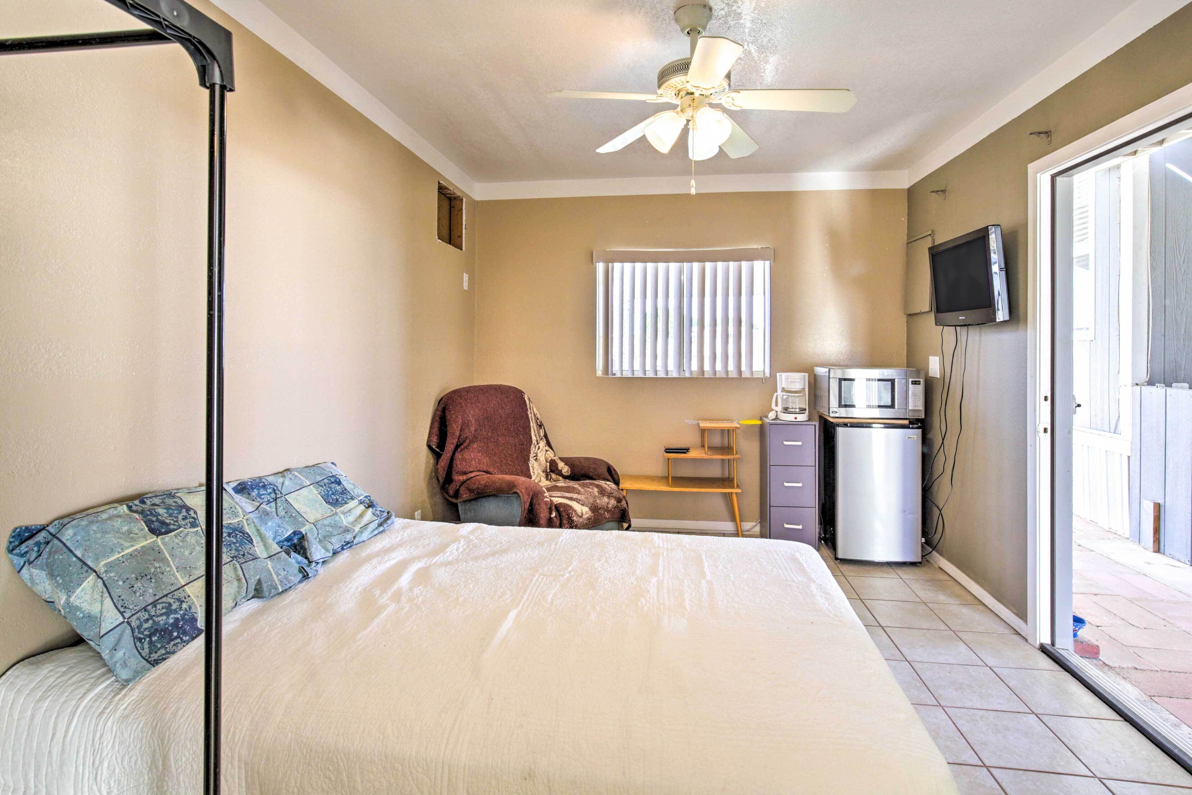 Une chambre à coucher comprenant un lit, une chaise, un bureau avec un ordinateur, une télévision et un réfrigérateur.