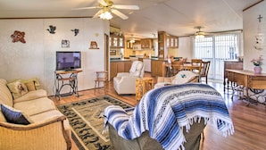 A spacious living room with a sofa, armchair, and a television. There is a dining area with a table and chairs, and a kitchen in the background. - Cozy Yuma Retreat w/ Furnished Patio & Grill! (Yuma)