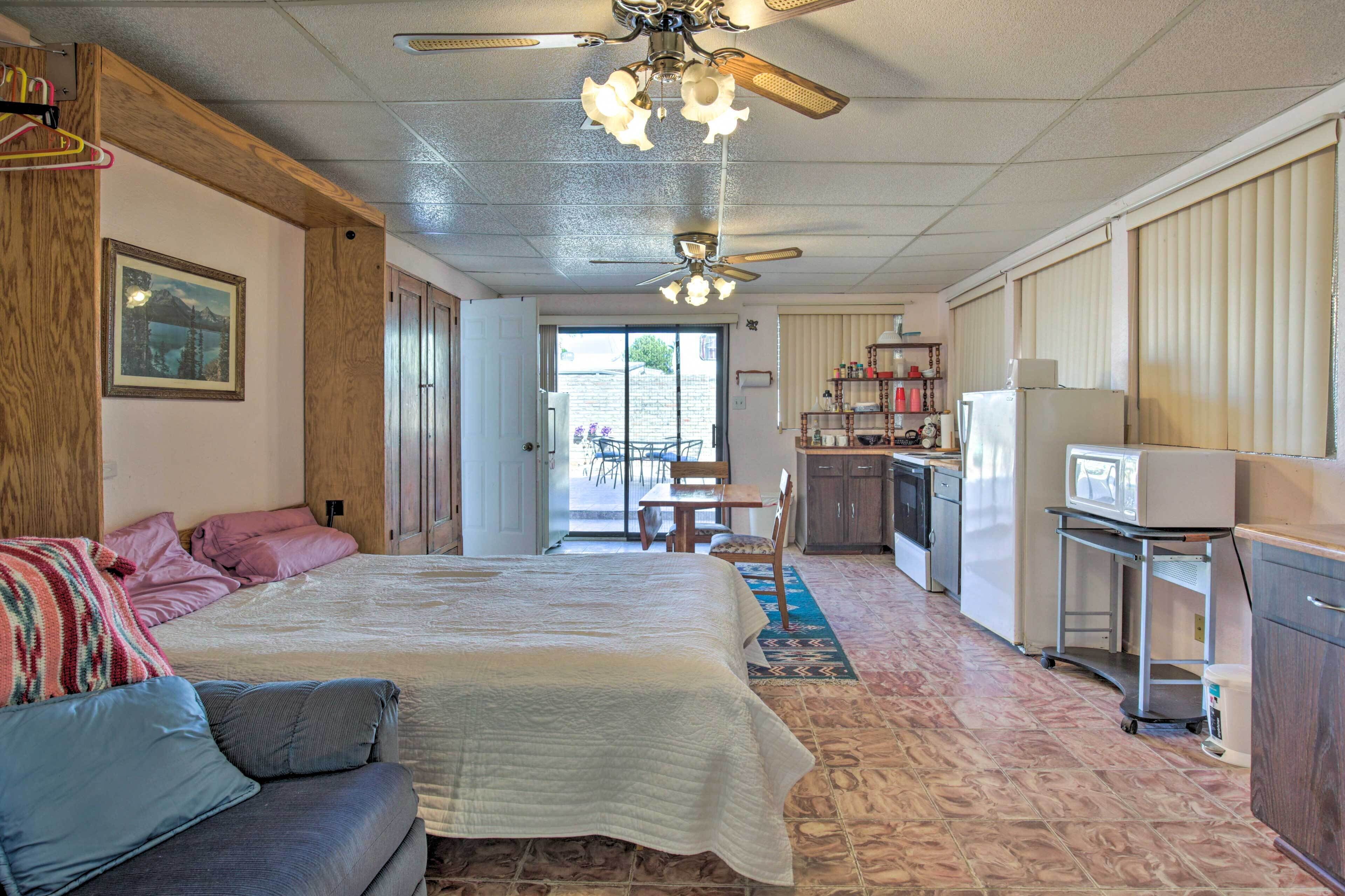 Un dormitorio con cama, sofá, ventilador de techo y una zona de cocina con refrigerador y microondas.