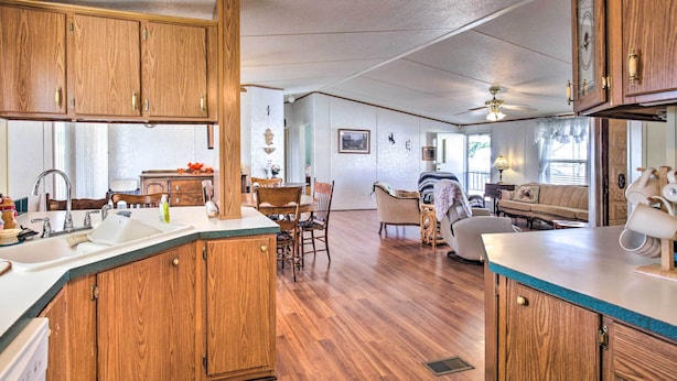 A spacious kitchen with wooden cabinets and a large island, a dining area with a table and chairs, and a living room with a sofa and a television. - Cozy Yuma Retreat w/ Furnished Patio & Grill! (Yuma)