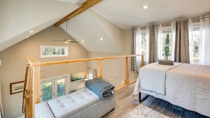 Een slaapkamer met een loft-plafond, een bed, een bankje en een raam met gordijnen.