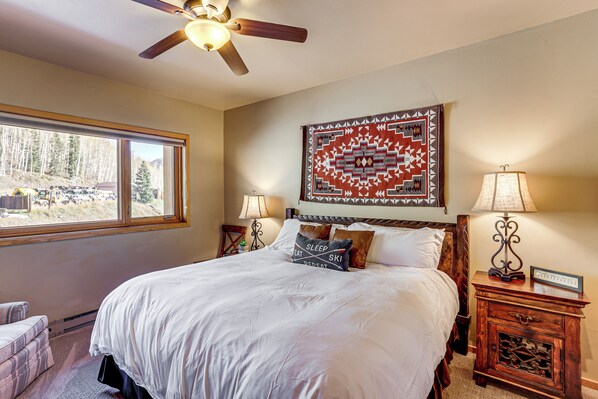 A neatly made bed with a white comforter and several pillows, a wooden headboard, a wall tapestry, two bedside lamps, and a nightstand with a clock.