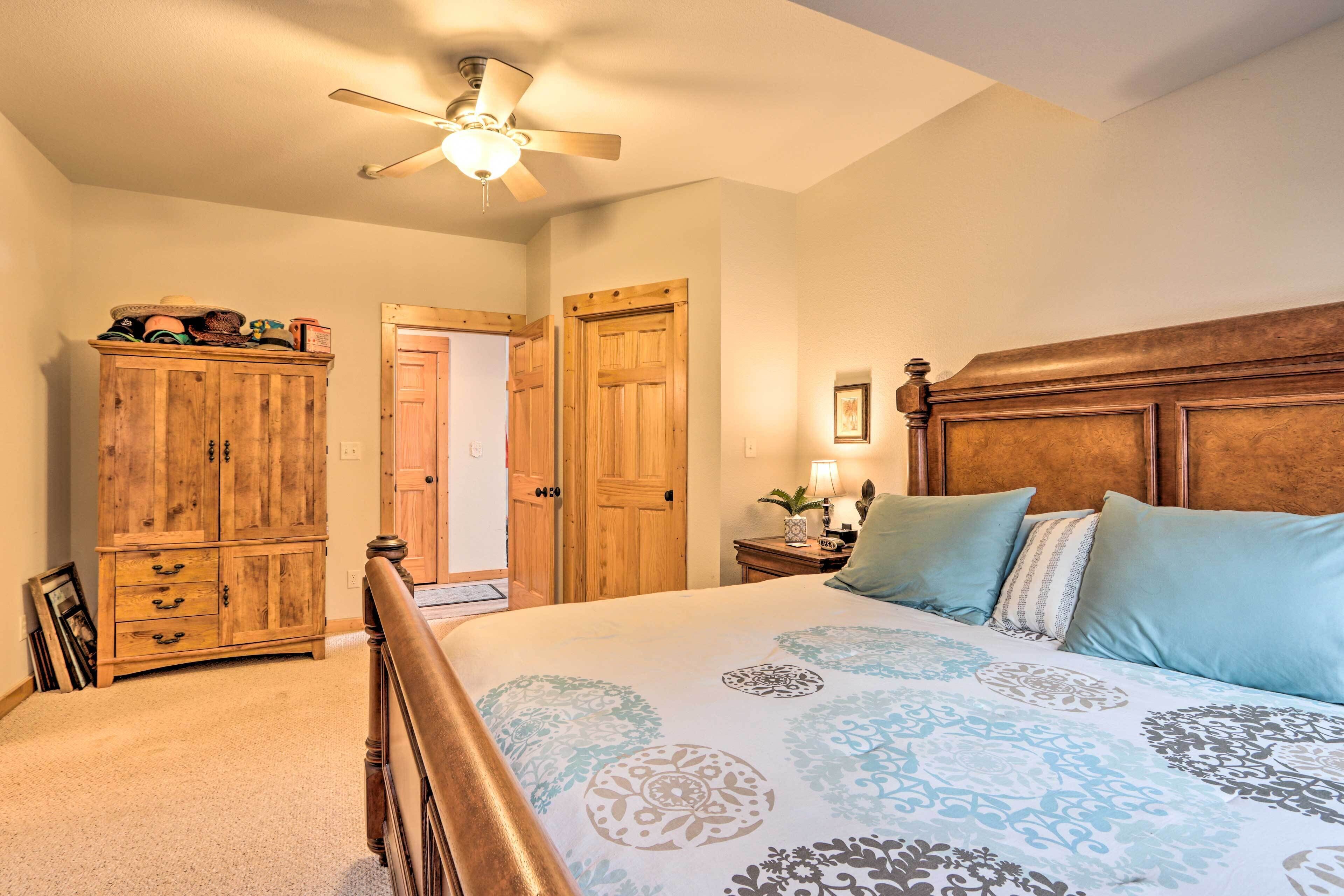 Une chambre à coucher avec une tête de lit en bois, un lit recouvert d’une literie à motifs, une armoire en bois et un ventilateur de plafond.