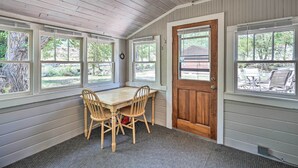 Une pièce avec une table et des chaises en bois, de grandes fenêtres et une porte.