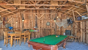 Une grange en bois avec une table de billard, des chaises et un jeu de fléchettes.