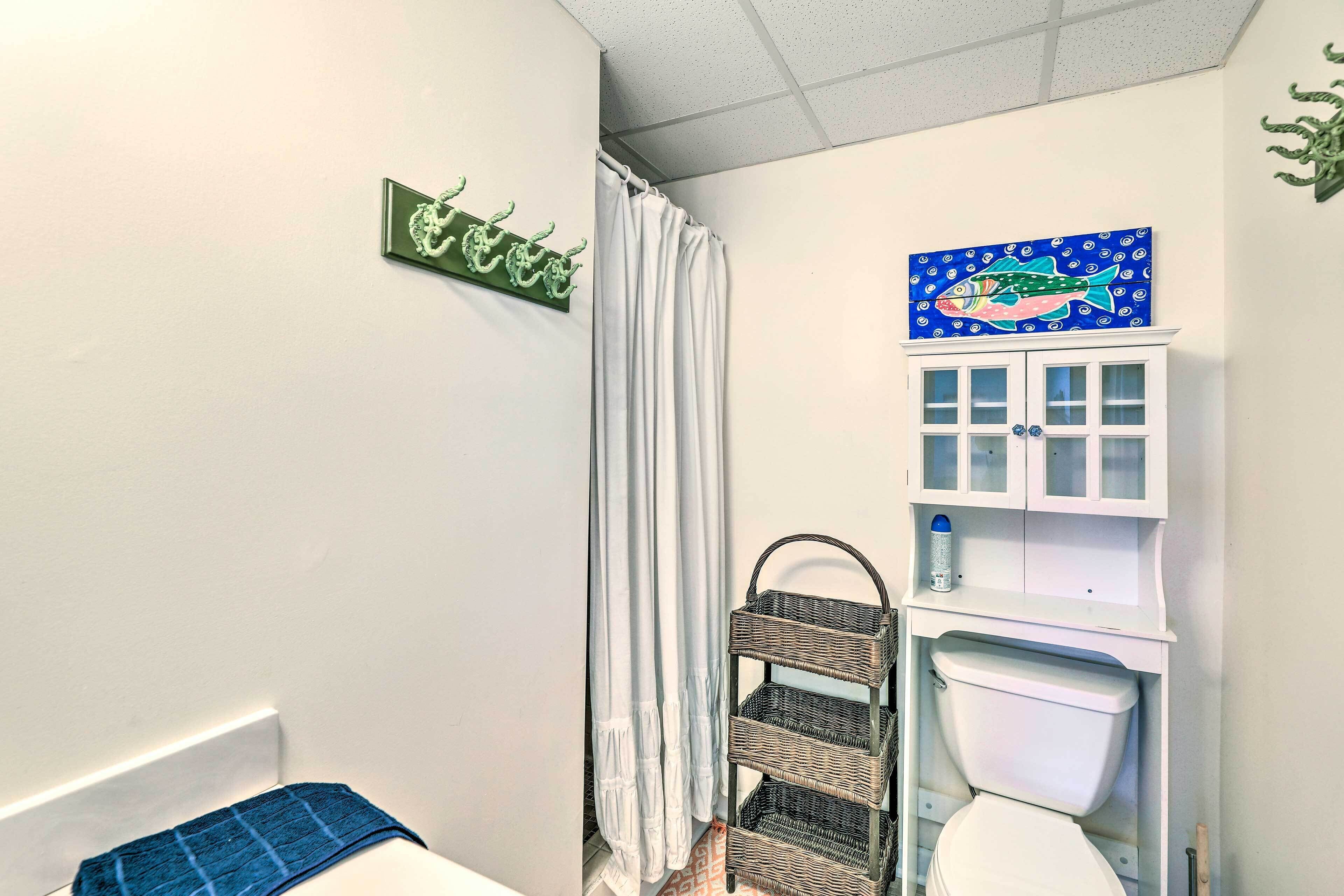 A bathroom with a white toilet, a wicker shelf, a blue fish painting, and a green wall decoration.