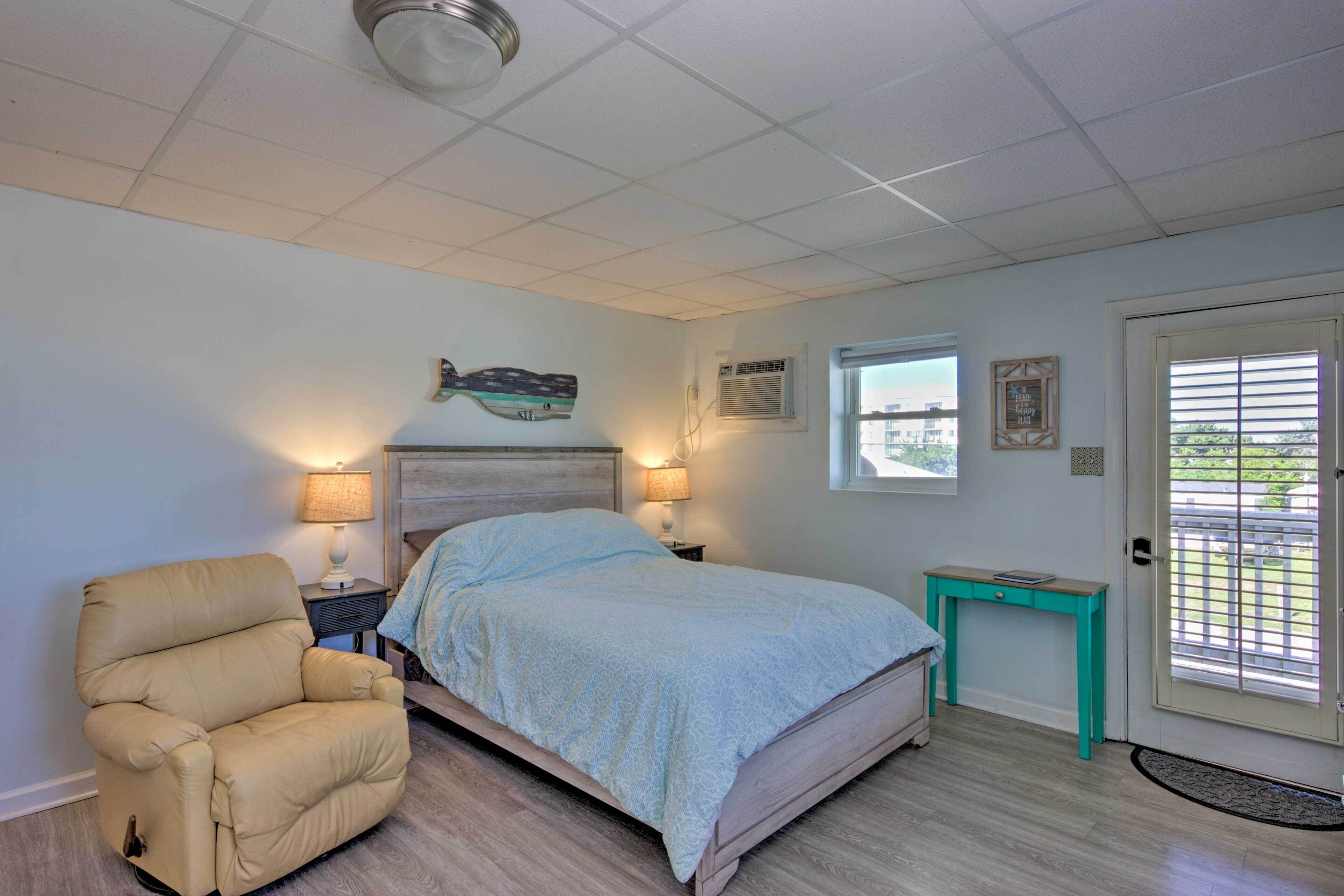 Une chambre à coucher comprenant un lit, un fauteuil inclinable, une table de chevet, une petite table et une porte donnant sur une vue agréable.