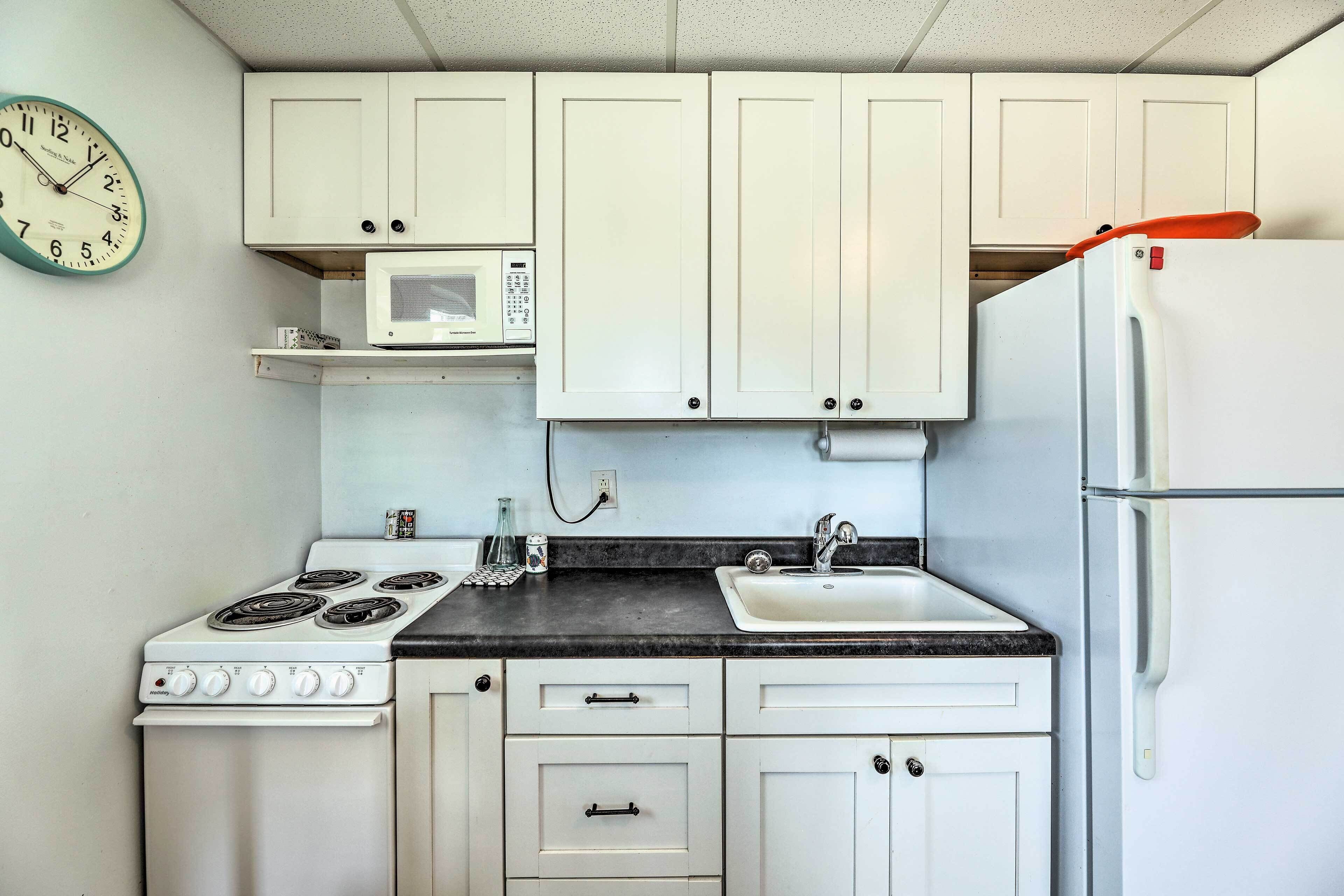 A kitchen with white cabinets, a stove, a microwave, and a refrigerator.
