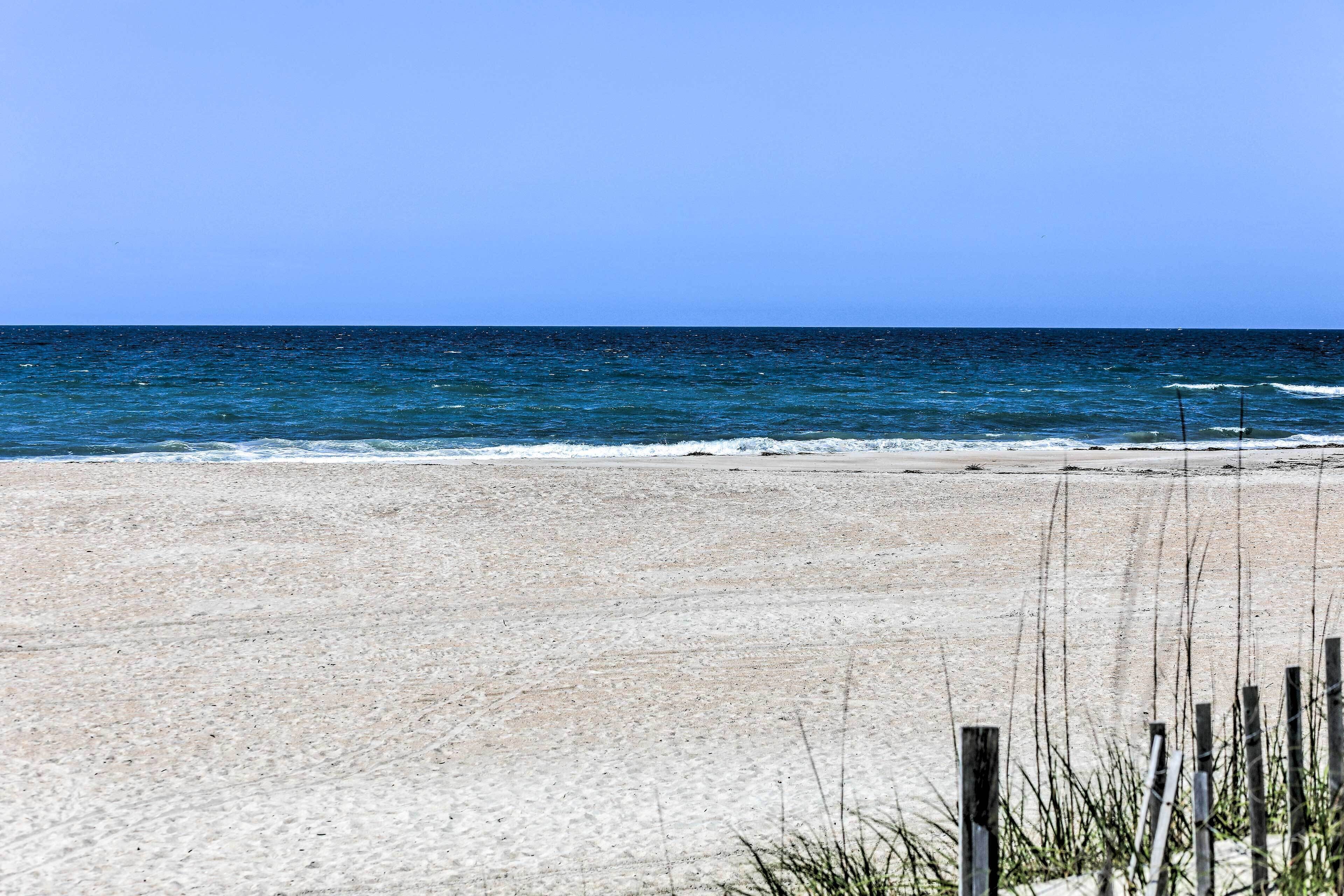 A sandy beach with a clear blue sky and ocean.