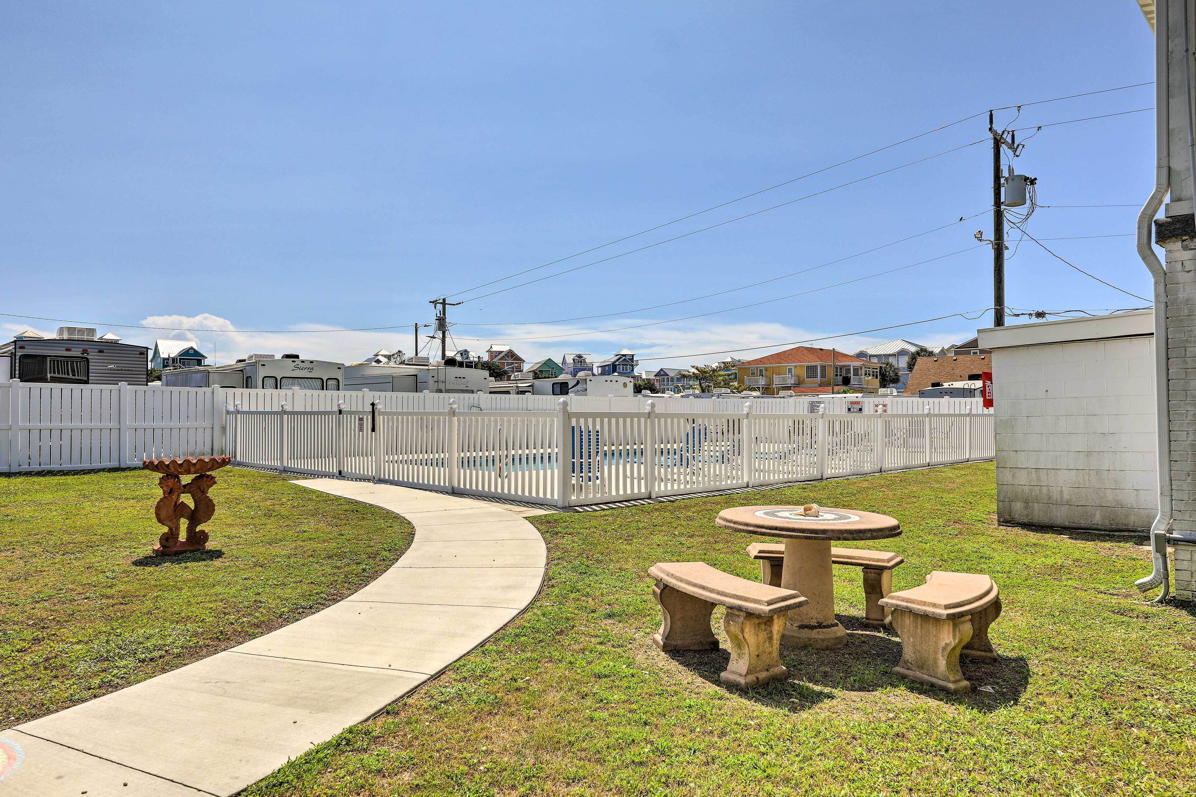 A fenced outdoor area with a picnic table and benches, a pathway, and a decorative sculpture.