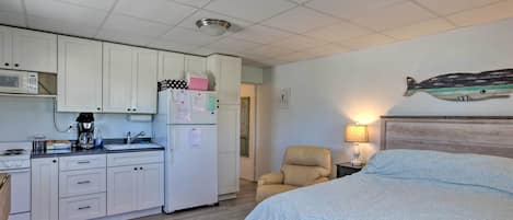 A compact room with a kitchenette, a bed, a chair, and a wall-mounted fish decoration.