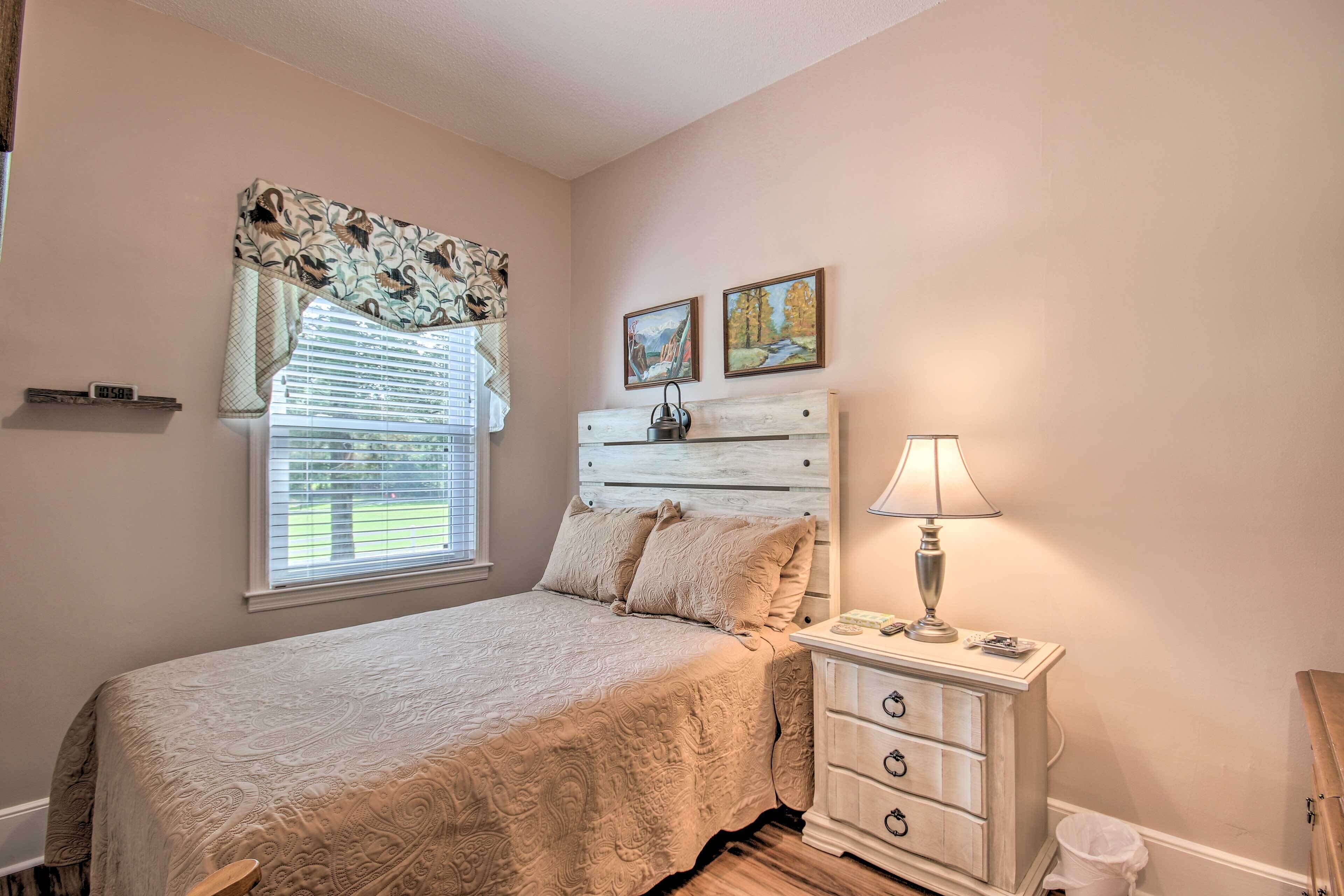 A bedroom with a bed, a nightstand with a lamp, a dresser, and two paintings on the wall.