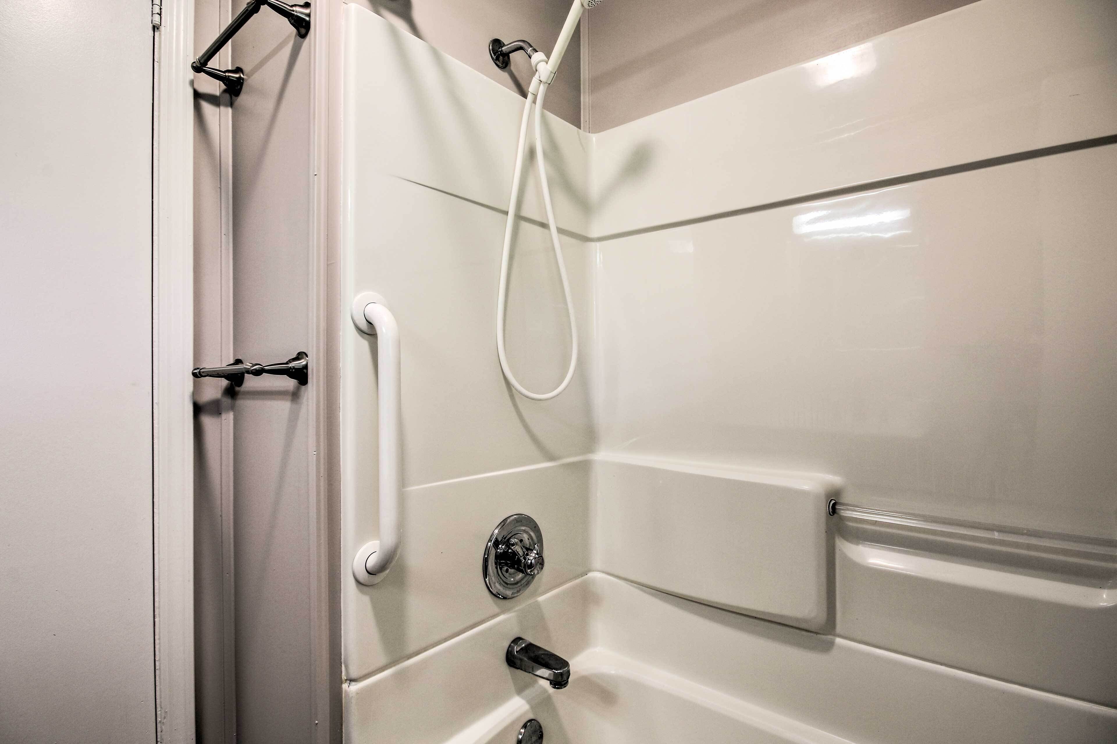 A bathroom with a white tiled wall, a shower with a handheld showerhead, and a white door.