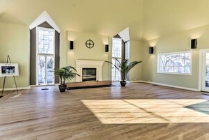 Una habitación amplia con techos altos, ventanas grandes, chimenea y plantas en macetas.