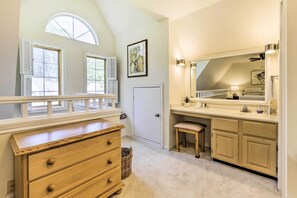 A bedroom with a large window, a wooden dresser, a vanity with a mirror, and a door. - Lovely Norwich Villa, On Golf Course w/ Amenities! (Norwich)