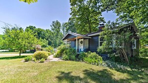 A house with a porch, surrounded by lush greenery and trees. - Stylish Dog-friendly Bungalow: Steps to Elk Lake (Elk Rapids)