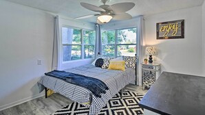 A bedroom with a bed, a ceiling fan, a window, a nightstand, and a wall decoration. - Stylish Dog-friendly Bungalow: Steps to Elk Lake (Elk Rapids)