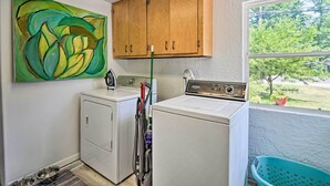 A laundry room with two white washing machines, a wooden cabinet above, and a green abstract painting on the wall. - Stylish Dog-friendly Bungalow: Steps to Elk Lake (Elk Rapids)