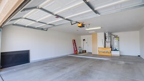 A spacious garage with a concrete floor, a closed garage door, and a water heater in the background. - Inviting Surprise Home With Covered Patio! (Surprise)