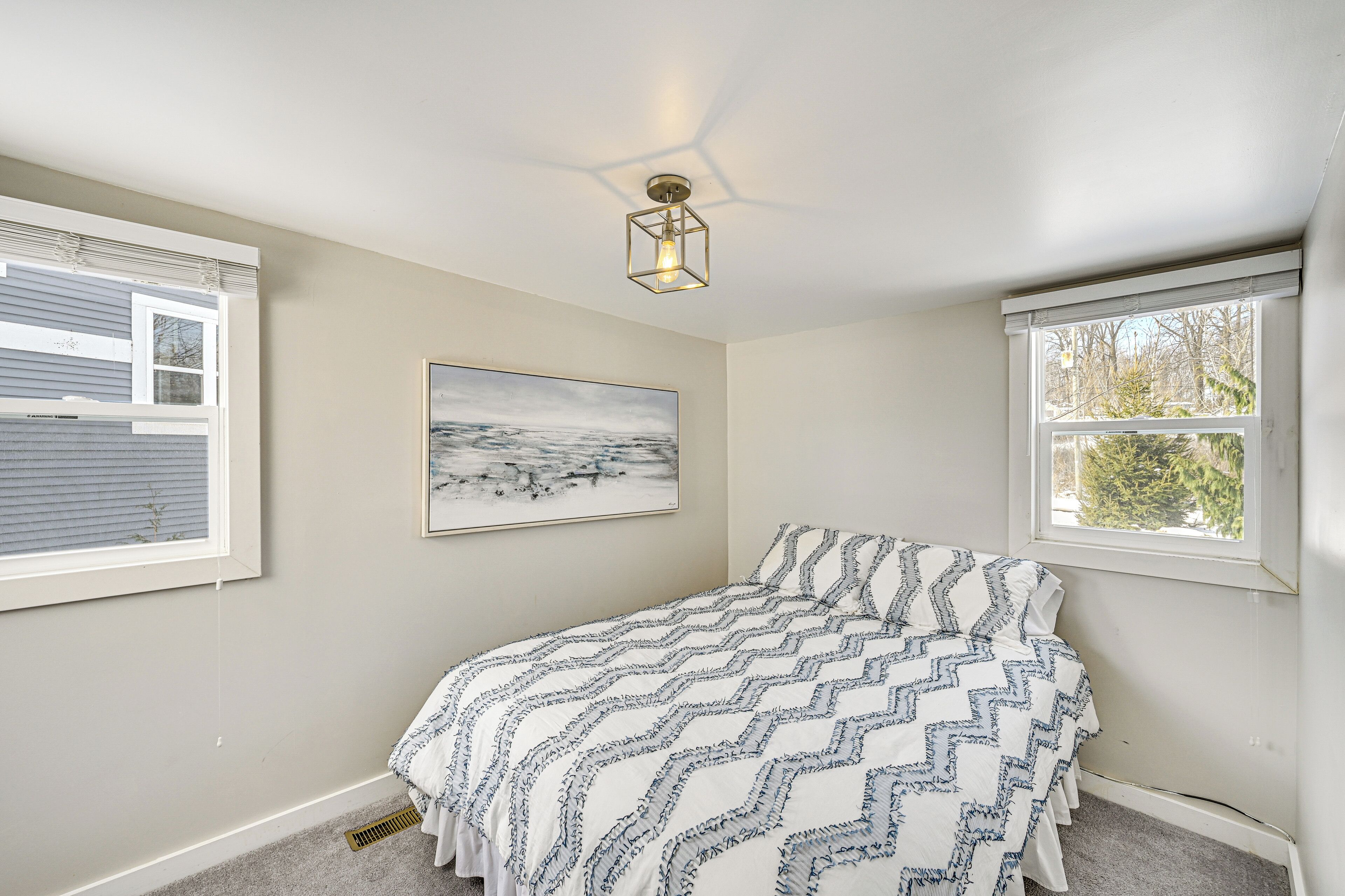 A bedroom with a bed, a ceiling light fixture, a window, and a painting on the wall.