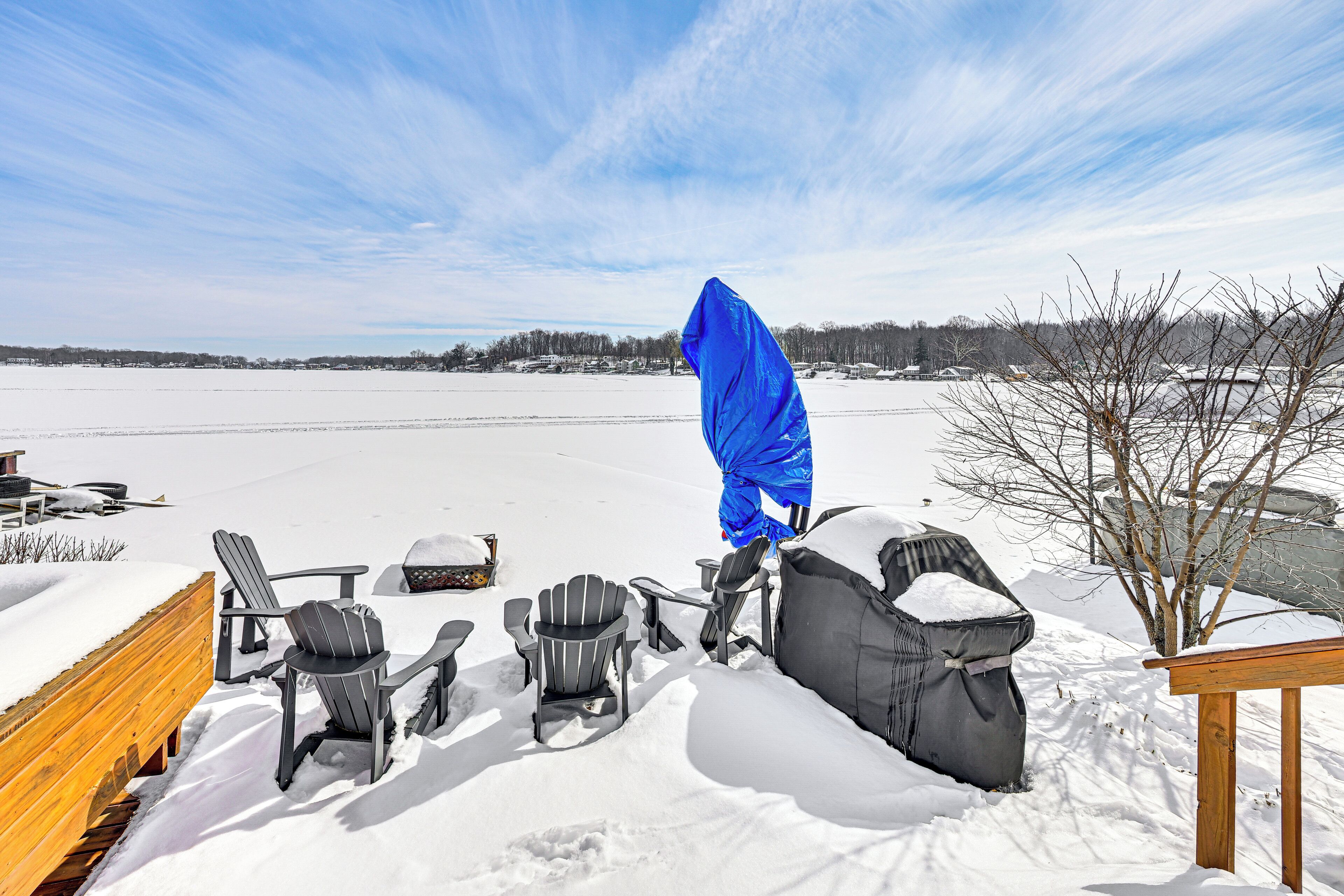 A snow-covered deck with Adirondack chairs and a wooden table.