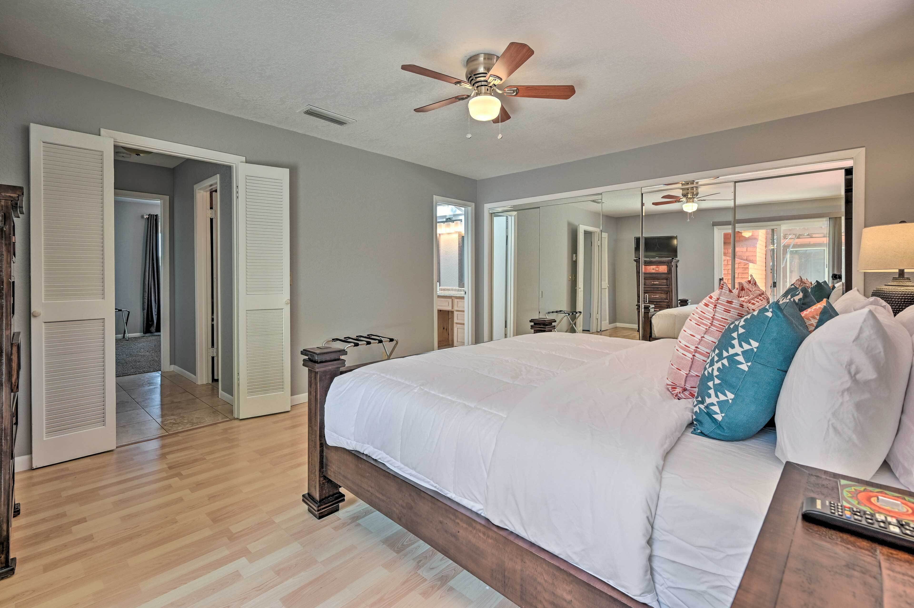 A bedroom with a large bed, a ceiling fan, a mirror, and a wooden floor.