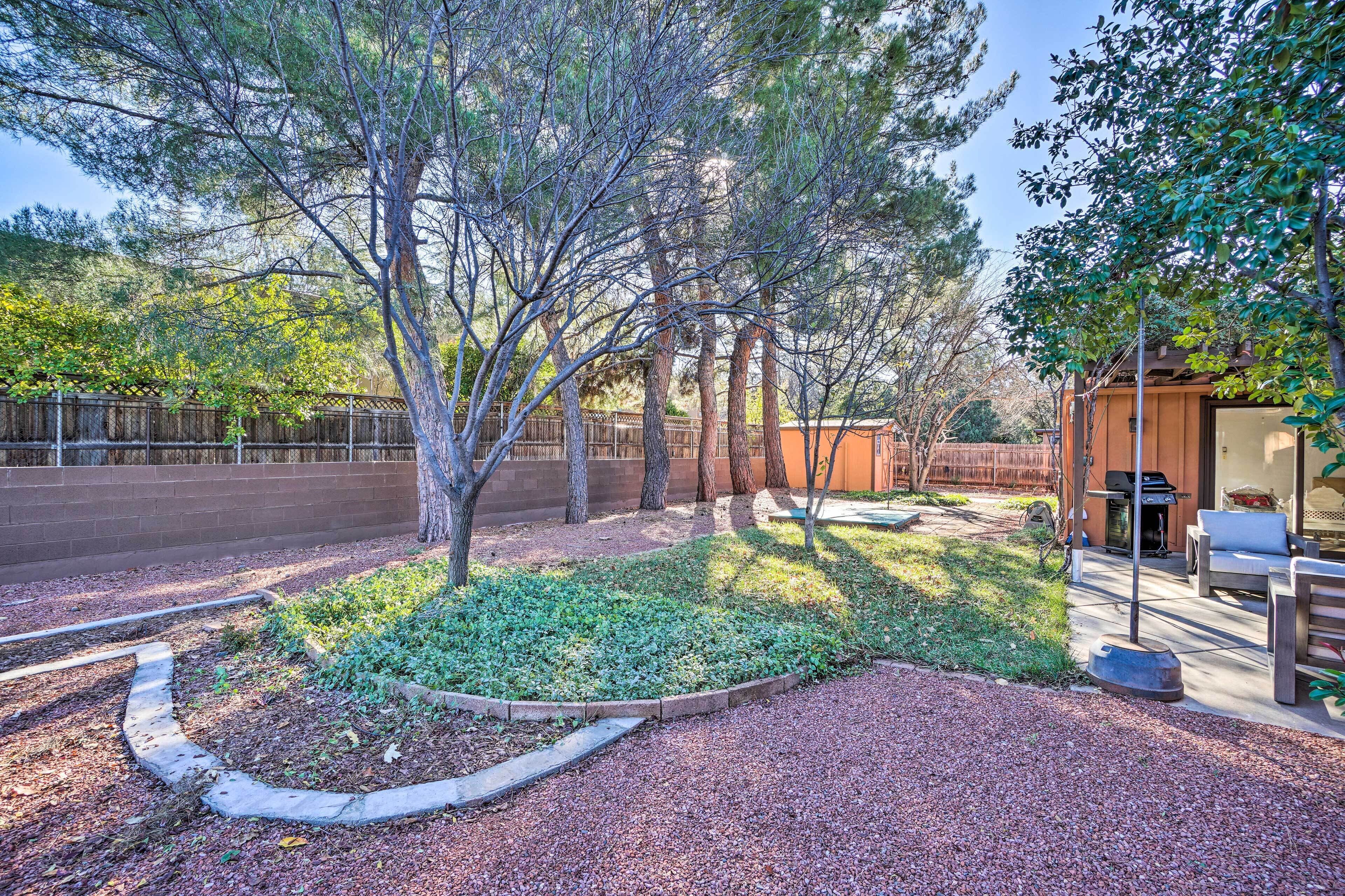 A landscaped backyard with a patio area, a wooden fence, and a barbecue grill.