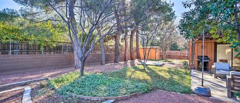 A landscaped backyard with a patio area, a wooden fence, and a barbecue grill.