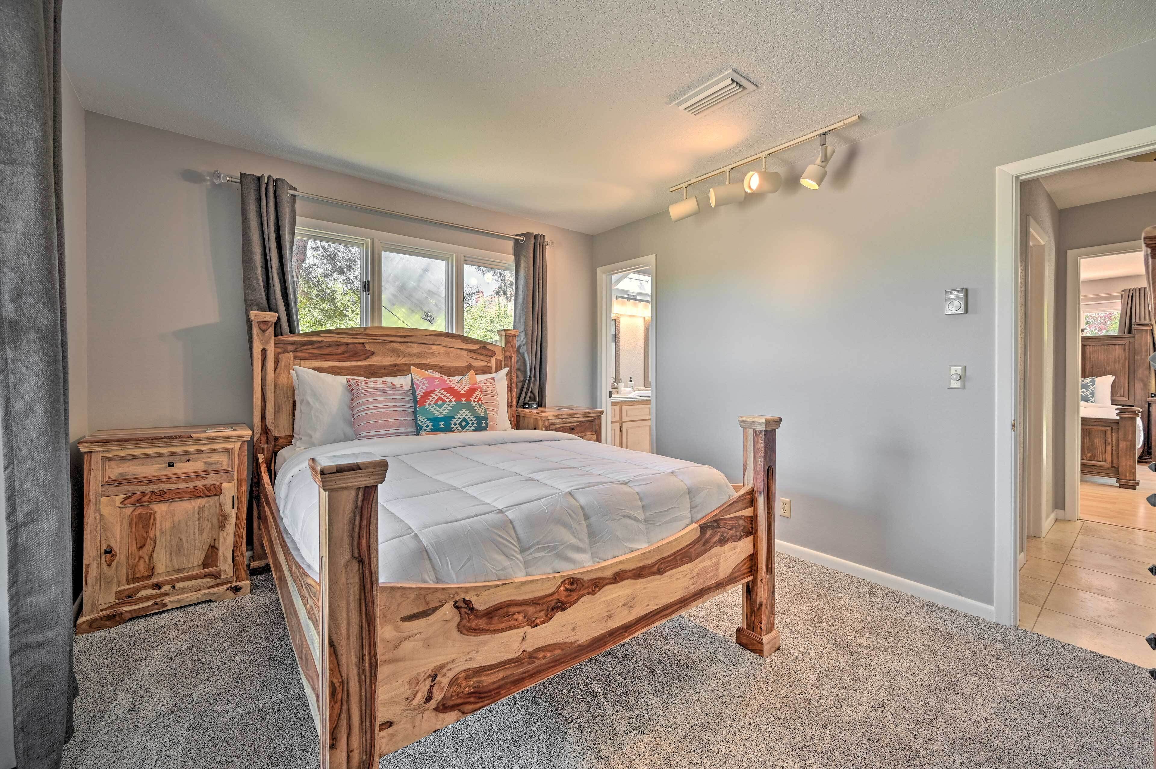 Une chambre à coucher avec un lit en bois, une table de chevet, une fenêtre avec des rideaux et un couloir menant à une salle de bain.