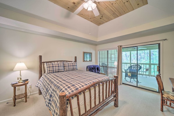 Quarto com uma cama grande, uma mesa de cabeceira, um ventilador de teto e vista para o exterior por uma porta de correr de vidro.