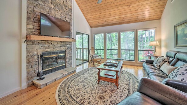 A spacious living room with a stone fireplace, wooden ceiling, and large windows offering a view of the outdoors. - Scenic Sapphire Condo w/ Deck + Gas Grill! (Sapphire)