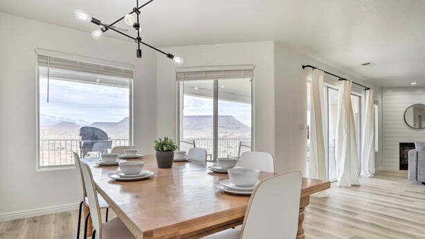 A dining area with a wooden table, white chairs, and a view of mountains through large windows. - Mtn-view Resort Condo, 5 Mi to Dtwn St George (St. George)