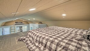 A bedroom with a checkered bedspread, a kitchenette in the background, and a sloped ceiling with recessed lighting. - Quaint Montezuma Cabin Near Lake Ponderosa! (Montezuma)