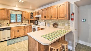 A kitchen with wooden cabinets, a large island with stools, a dishwasher, and a window with blinds. - Walkable Lake Elkhart Apt: Dine, Shop, Swim! (Elkhart Lake)