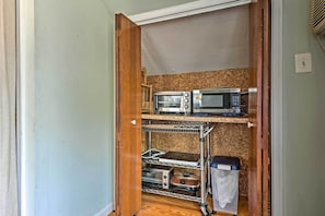 A compact kitchen with a microwave, toaster, and a small oven on a metal shelf.