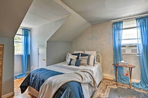 A bedroom with a sloped ceiling, a bed with a patterned bedspread, a bedside table with a tissue box, and blue curtains.