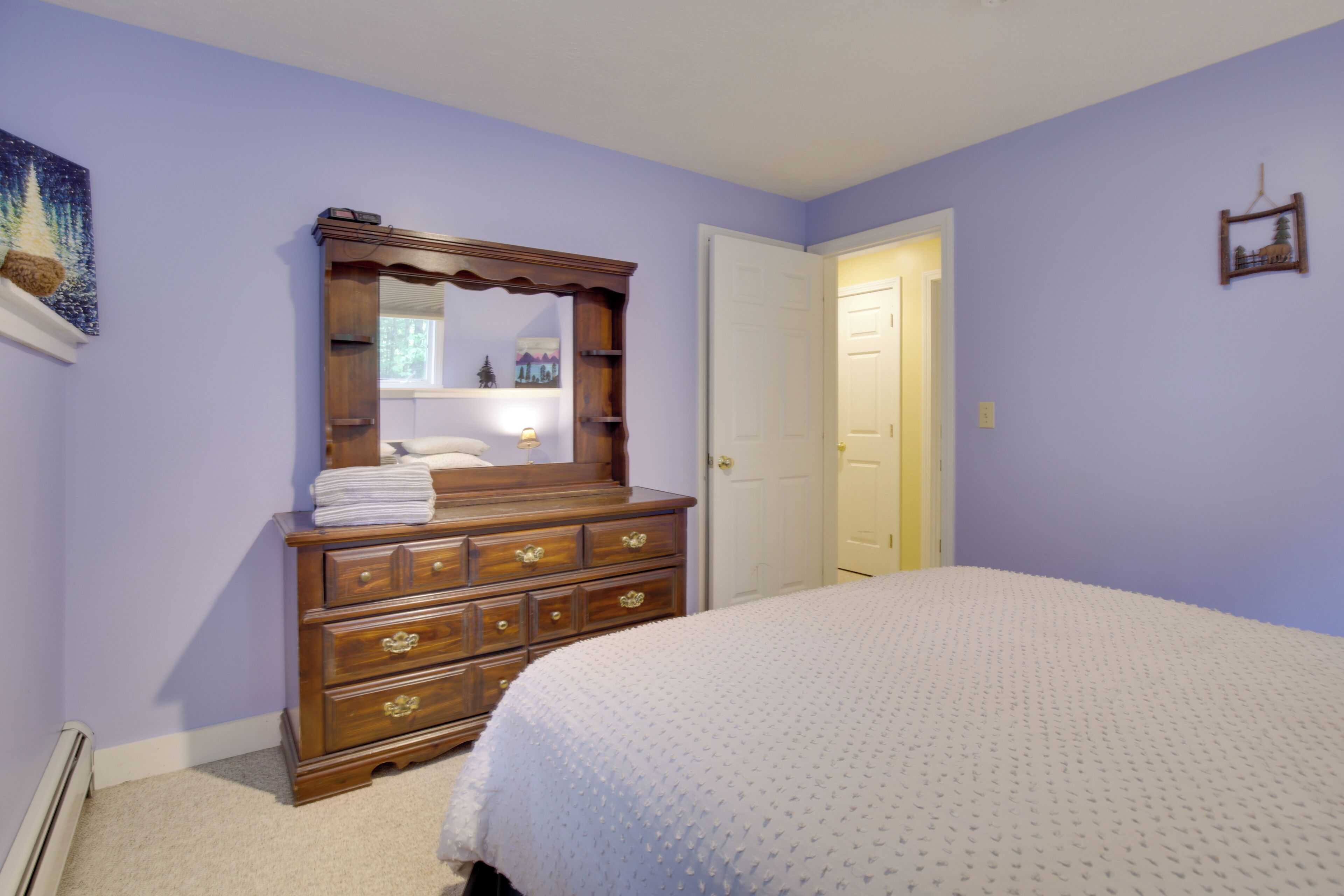 A bedroom with a large bed, a wooden dresser with drawers, a mirror, and a door.
