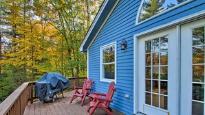 Une maison bleue avec une terrasse, deux chaises Adirondack rouges et un barbecue.