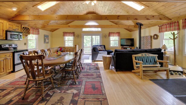 Un vaste espace de vie doté d’un plafond en bois, d’une table à manger avec des chaises, d’un canapé et d’un téléviseur.