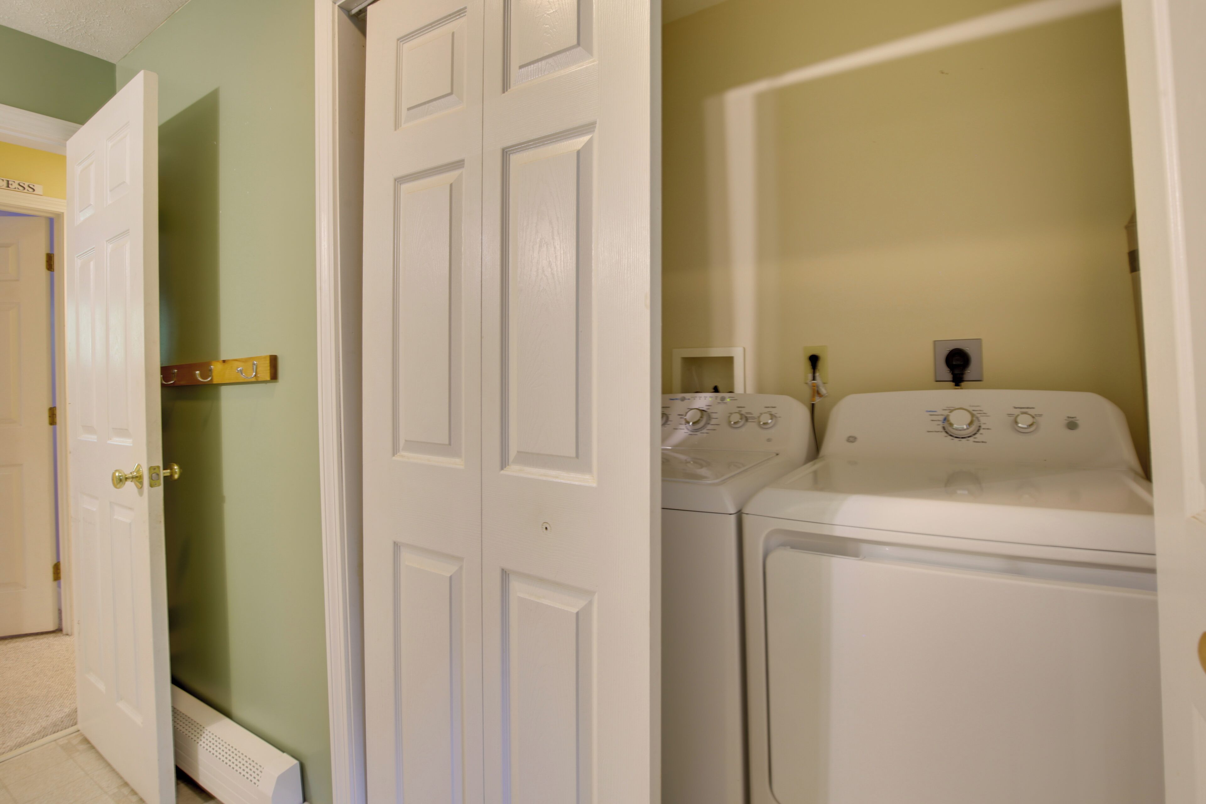 A laundry room with two white washers and dryers, a radiator, and a door with a brass handle.