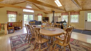 Un salon spacieux avec un plafond en bois, une table à manger ronde entourée de chaises, une cheminée et un téléviseur.