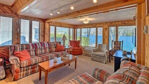 L’intérieur chaleureux d’un chalet avec un canapé à carreaux, des fauteuils et une table basse en bois. De grandes fenêtres offrent une vue sur l’extérieur.