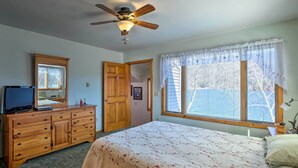 Une chambre à coucher avec un lit, une commode, un ventilateur de plafond et une fenêtre avec des rideaux.
