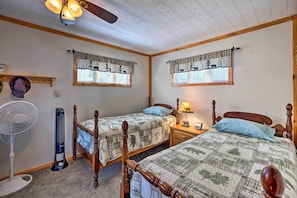 A bedroom with two wooden beds, a standing fan, a heater, and a ceiling fan.