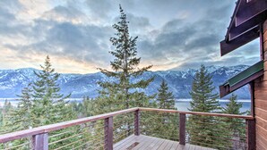 Une terrasse en bois avec une rambarde en métal, offrant une vue sur un paysage montagneux et une étendue d’eau.