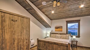 Une chambre avec un lit en bois, une grande armoire, une fenêtre donnant sur les montagnes et un ventilateur de plafond.
