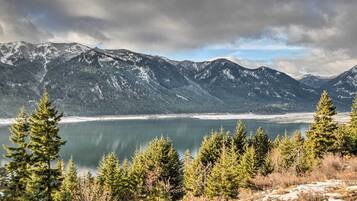 Un paysage montagneux avec un lac, entouré d’arbres à feuilles persistantes et de sommets enneigés.