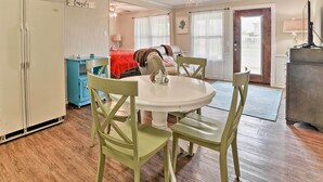 A dining area with a white table and green chairs, a blue cabinet, and a red bed in the background. - Rockport Bayfront Studio w/ Patio: 'casa Familia' (Rockport)